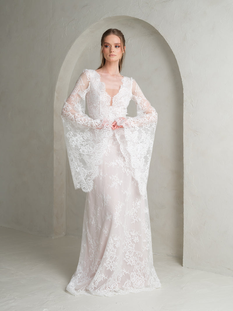 Boho bride wearing a white lace wedding dress with long sleeves standing in an archway wedding