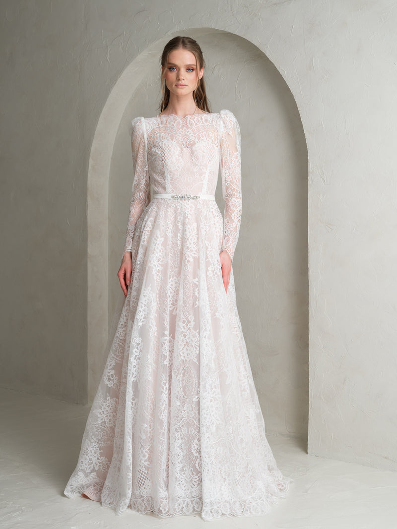 Classic Bride wearing a long-sleeve lace wedding dress with belt in a neutral setting