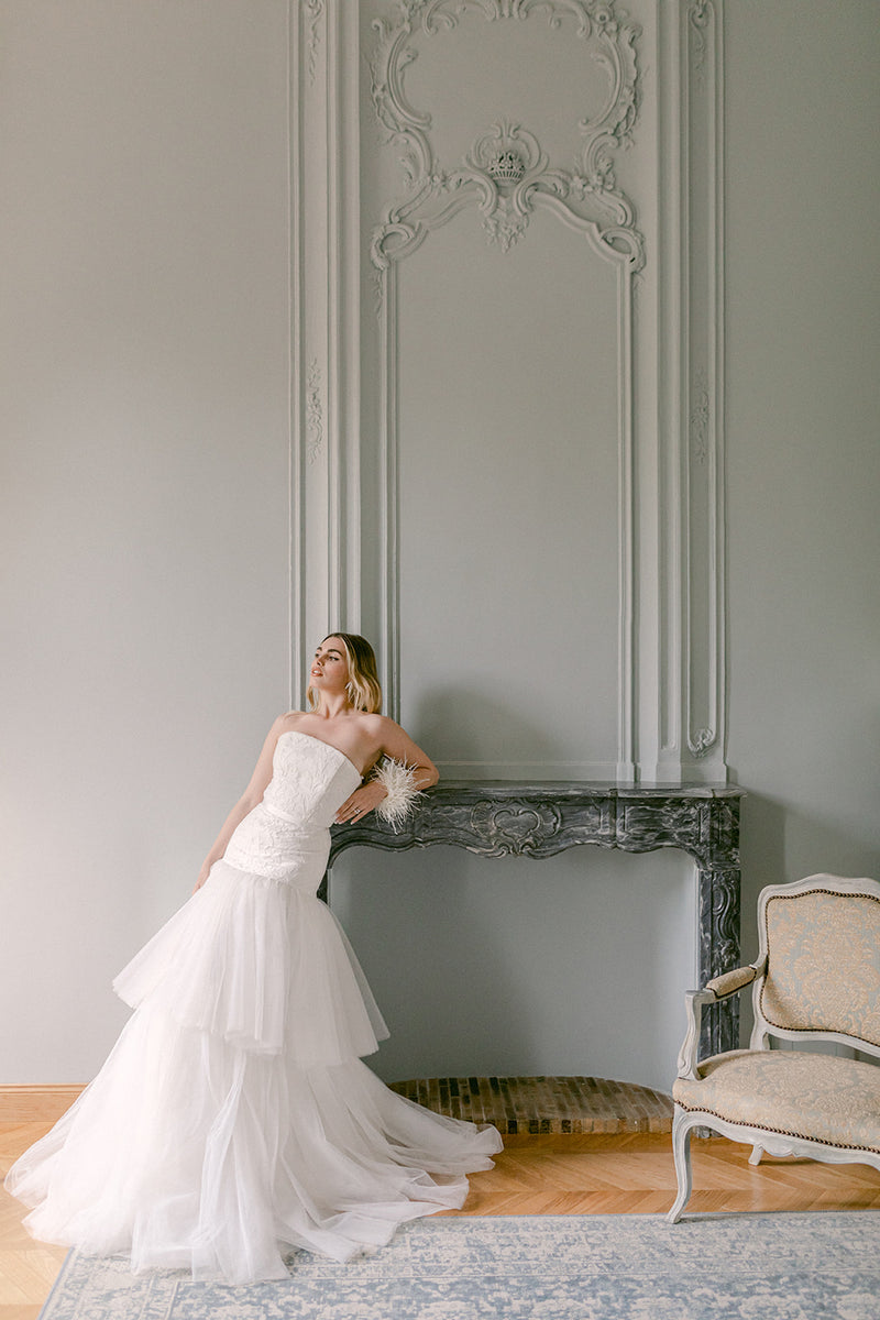 Bride in a white mermaid wedding dress lace and tulle standing in an elegant room with ornate wall designs.